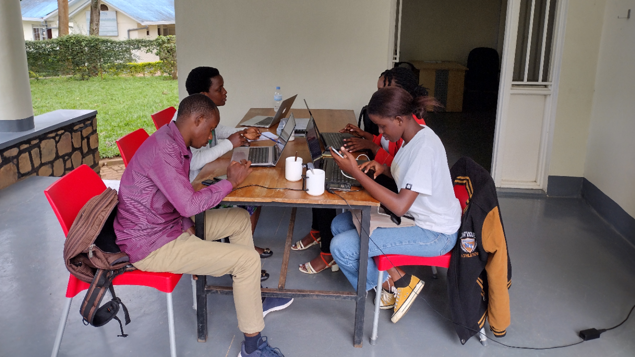 Four Bridge2Rwanda interns sitting at a table on a patio, curating agriculture resources in Kinyarwanda